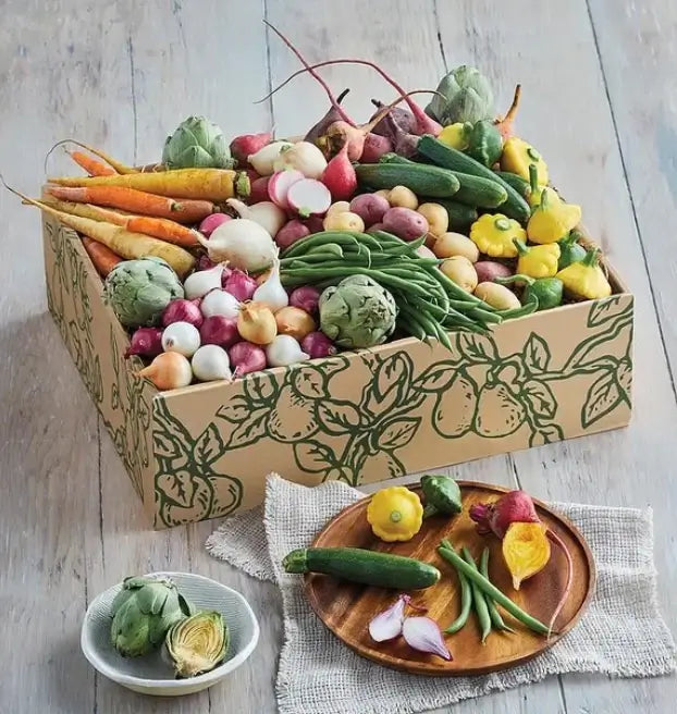 Box of assorted fresh vegetables on a wooden surface with some displayed on a plate.