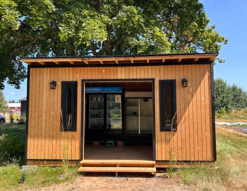 Overcast Farms farm stand, with a wooden outside and roof, along with two coolers filled with veggies.